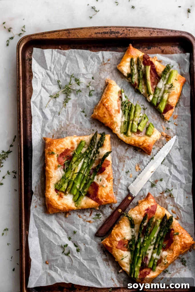 Asparagus Tarts with Bacon and Gruyere - The easiest appetizer or side you'll ever whip up! Made with store-bought puff pastry, fresh asparagus, bacon, and lots of cheese! It's a flavor explosion of sweet, smoky bacon, asparagus, melty cheese, and crisp puff pastry. #asparagus #easterrecipes #asparagus #easyrecipes #easyappetizers #easyeasterrecipes #puffpastry #bacon #gruyere #bluebowlrecipes | bluebowlrecipes.com Several asparagus tarts with bacon and gruyere arranged on a baking sheet, freshly out of the oven.