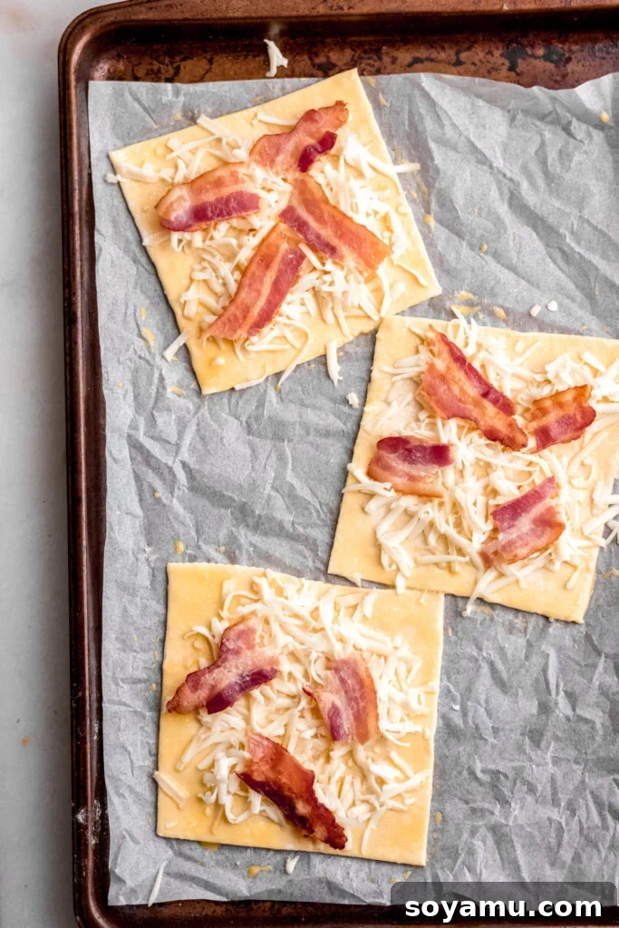 Asparagus Tarts with Bacon and Gruyere - The easiest appetizer or side you'll ever whip up! Made with store-bought puff pastry, fresh asparagus, bacon, and lots of cheese! It's a flavor explosion of sweet, smoky bacon, asparagus, melty cheese, and crisp puff pastry. #asparagus #easterrecipes #asparagus #easyrecipes #easyappetizers #easyeasterrecipes #puffpastry #bacon #gruyere #bluebowlrecipes | bluebowlrecipes.com Puff pastry squares topped with grated Gruyere cheese and crumbled bacon, ready for asparagus.