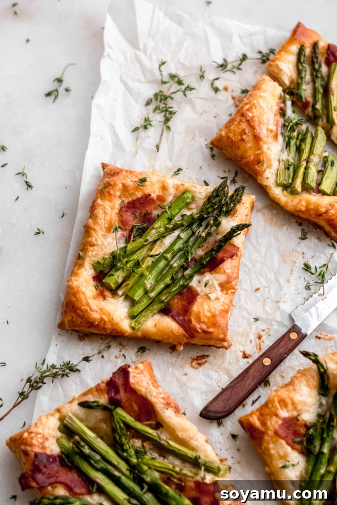 Asparagus Tarts with Bacon and Gruyere - The easiest appetizer or side you'll ever whip up! Made with store-bought puff pastry, fresh asparagus, bacon, and lots of cheese! It's a flavor explosion of sweet, smoky bacon, asparagus, melty cheese, and crisp puff pastry. #asparagus #easterrecipes #asparagus #easyrecipes #easyappetizers #easyeasterrecipes #puffpastry #bacon #gruyere #bluebowlrecipes | bluebowlrecipes.com A trio of asparagus tarts with bacon and gruyere on a white plate, garnished with fresh herbs.