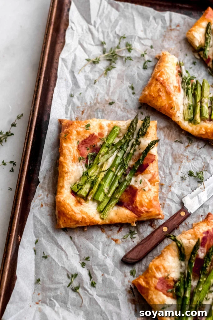 Asparagus Tarts with Bacon and Gruyere - The easiest appetizer or side you'll ever whip up! Made with store-bought puff pastry, fresh asparagus, bacon, and lots of cheese! It's a flavor explosion of sweet, smoky bacon, asparagus, melty cheese, and crisp puff pastry. #asparagus #easterrecipes #asparagus #easyrecipes #easyappetizers #easyeasterrecipes #puffpastry #bacon #gruyere #bluebowlrecipes | bluebowlrecipes.com Several asparagus tarts with bacon and gruyere stacked on a serving tray.