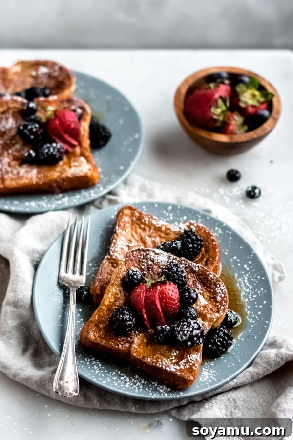 Gourmet Brioche French Toast Plating for Brunch Beautifully plated brioche French Toast adorned with fresh mixed berries and a dusting of powdered sugar, presented on a light-colored dish.