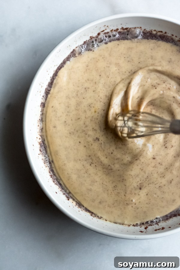 Preparation of French Toast Custard Batter Close-up shot of a whisk actively mixing French Toast batter in a clear glass bowl, showcasing a smooth, spiced custard.