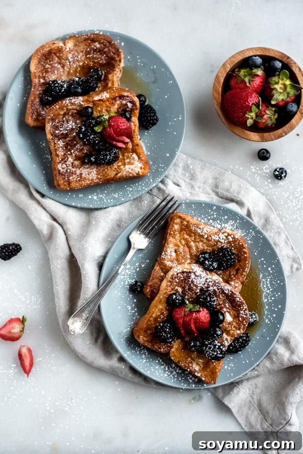 Plated Brioche French Toast with Fresh Berries A stack of fluffy brioche French Toast served on a white plate, garnished with an abundance of fresh mixed berries and a delicate dusting of powdered sugar.