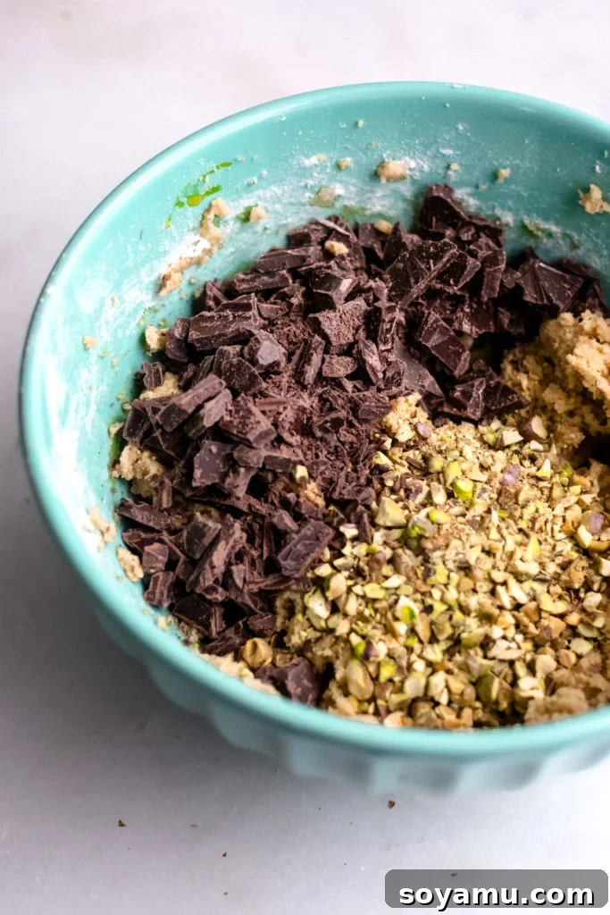 Chocolate chunks and chopped pistachios being mixed into cookie dough.