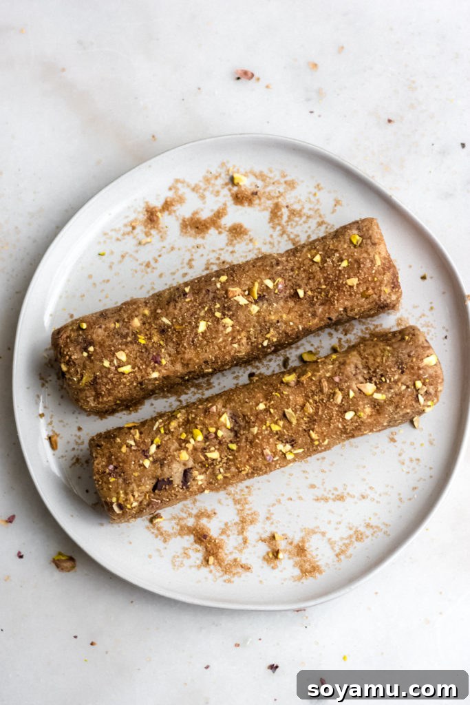 Two cookie dough logs rolled and coated with pistachios and sugar.