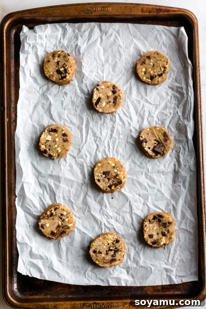Unbaked chocolate pistachio cookies neatly arranged on a parchment-lined baking sheet.