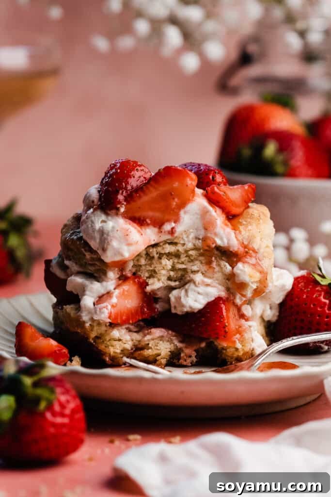 Sun-Kissed Strawberry Shortcakes with Dreamy Whipped Cream 3 A close-up on a strawberry shortcake on a plate, with a bite missing to show the fluffy inside of the biscuit.
