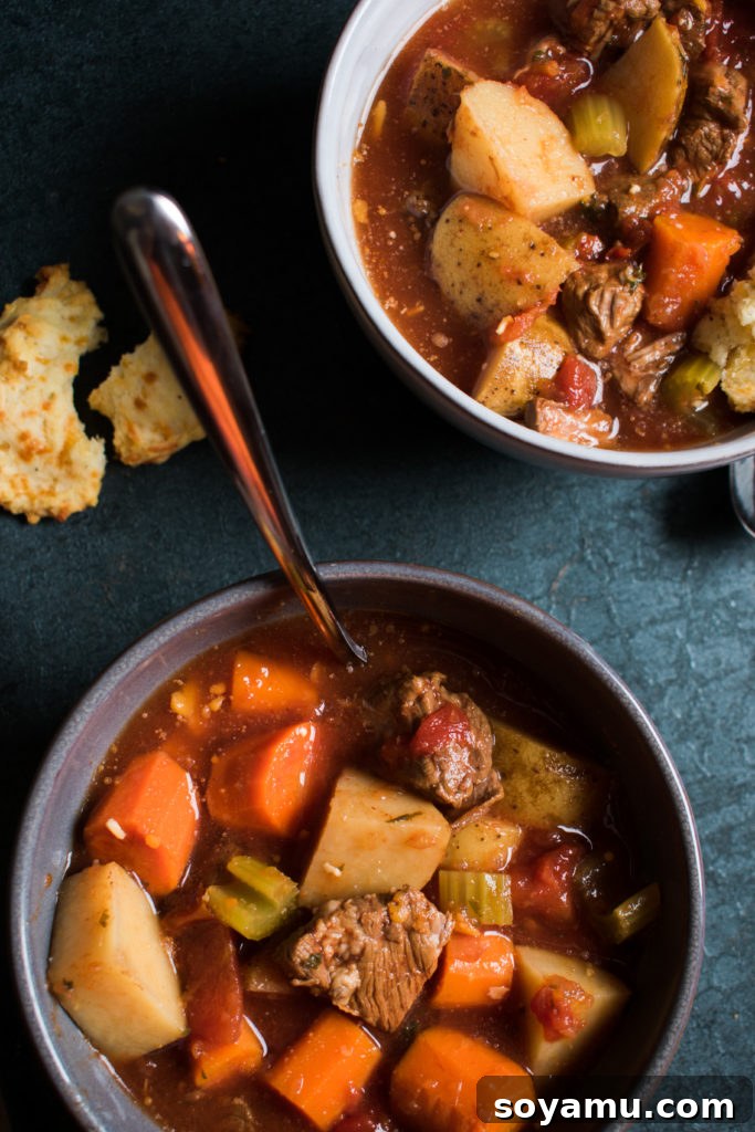 A beautifully set table with a bowl of vegetable beef soup and fresh biscuits.