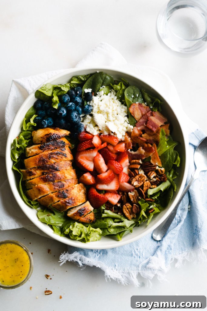 Strawberry Bacon Summer Salad with Poppyseed Perfection 5 Various ingredients for a strawberry summer salad, including berries, greens, chicken, and feta, arranged in a bowl.