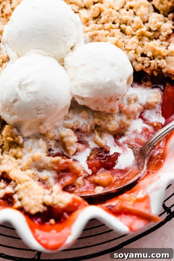 Easy One Bowl Strawberry Rhubarb Crumble 3 A close-up shot of a serving spoon scooping a portion of the warm, bubbly Strawberry Rhubarb Crumble from the baking dish, highlighting its juicy fruit filling and golden topping.