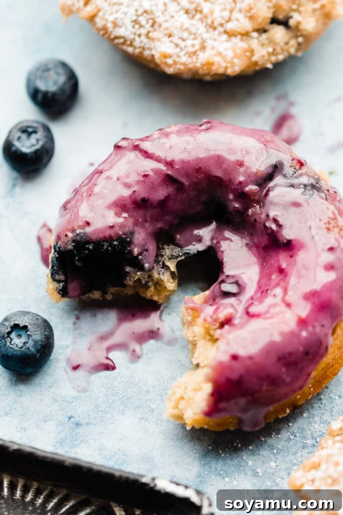 A close-up of a blueberry glazed donut with a bite missing, showcasing its soft interior.