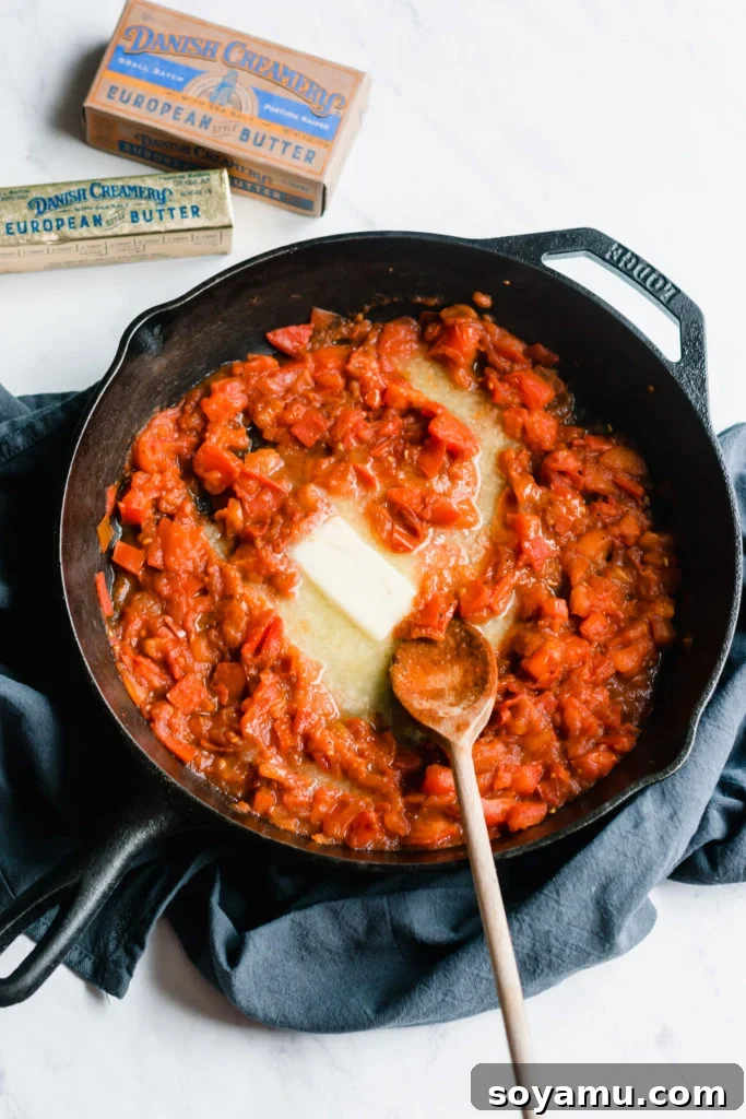 Melting Butter into Tomato Sauce Cast iron skillet with chopped tomatoes and a stick of melting butter.