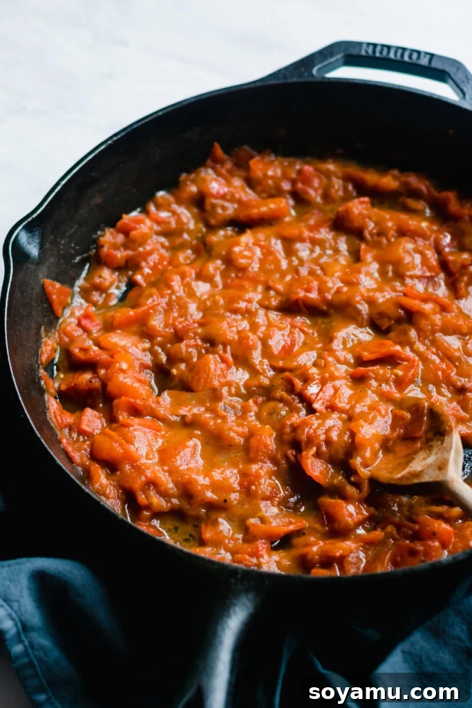 Simmering Garlic Butter Tomato Sauce Tomatoes cooking with butter in a cast iron skillet, bubbling gently.