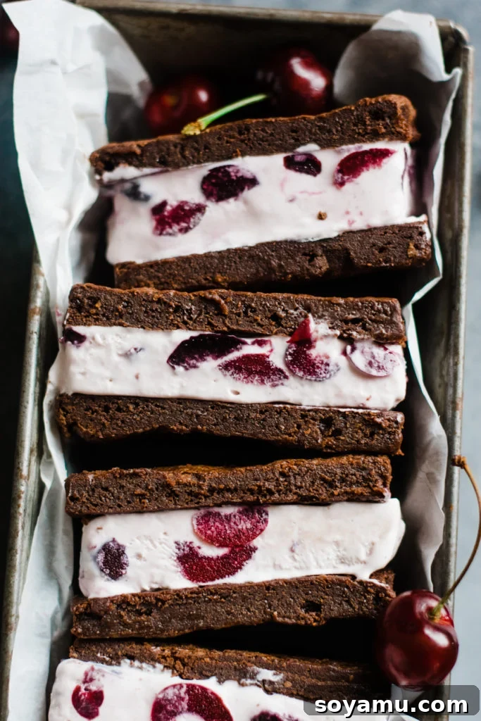 Handcrafted Black Forest Ice Cream Sandwiches 7 Several Black Forest ice cream sandwiches arranged neatly in a tin, with some partially unwrapped to show the inner layers of brownie and cherry ice cream.
