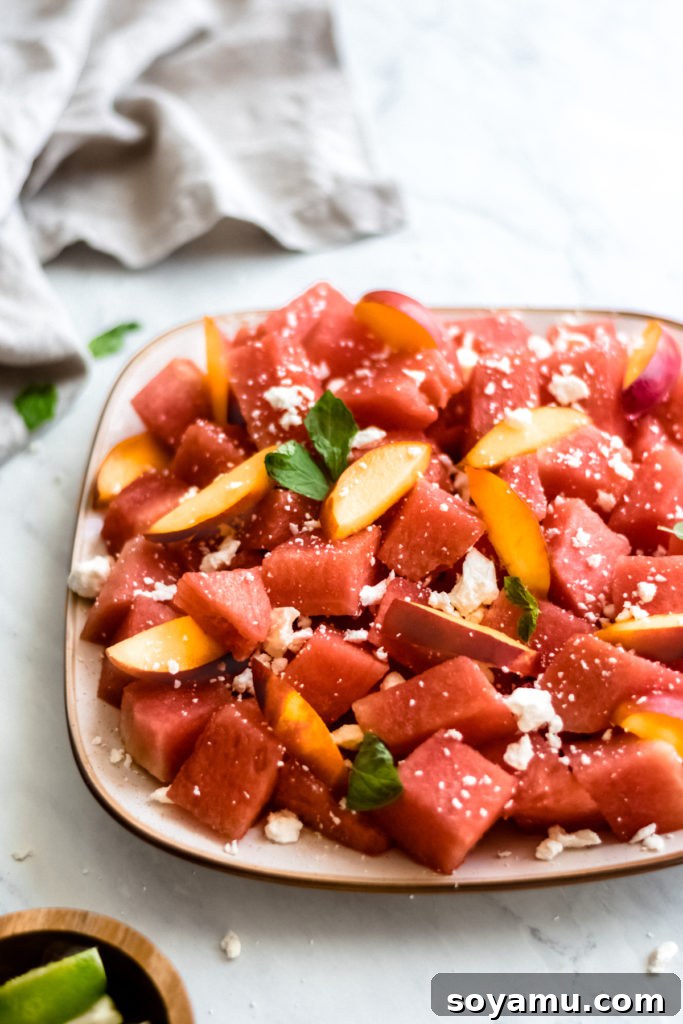 Close-up of watermelon nectarine salad with feta and honey lime dressing on a white plate, ready to be served.