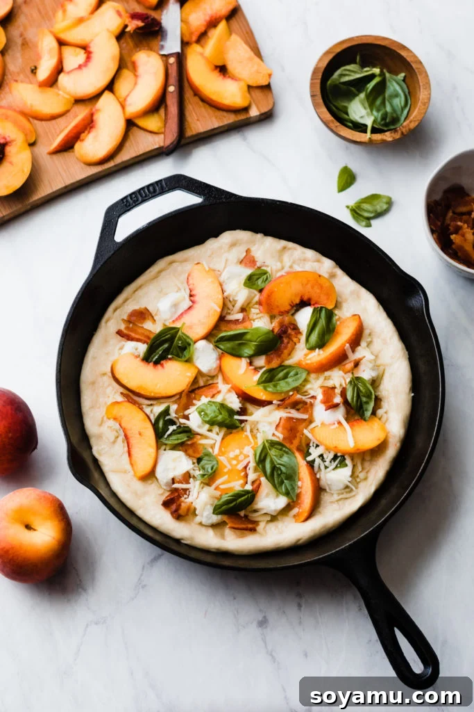 Unbaked peach pizza assembled on dough in a cast iron skillet, ready for the oven.
