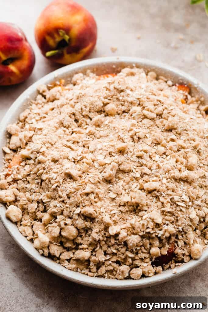 Heavenly Brown Butter Peach Crisp 8 The crisp topping generously scattered over the peach filling in a baking dish, ready for baking.