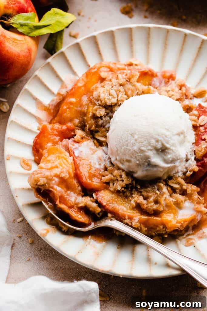 Heavenly Brown Butter Peach Crisp 10 A close-up shot of a plate of peach crisp with a spoon digging into the warm, juicy filling and crunchy topping.