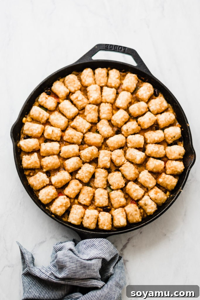 Tater Tot Hot Dish Ready for the Oven Frozen tater tots evenly spread over the creamy, savory filling in a cast iron skillet, ready to be baked to golden perfection.