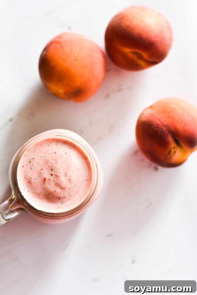 Effortless Vitality: 4 Wholesome Smoothie Creations 6 A refreshing peach and strawberry smoothie in a tall glass, with fresh peach slices as garnish.
