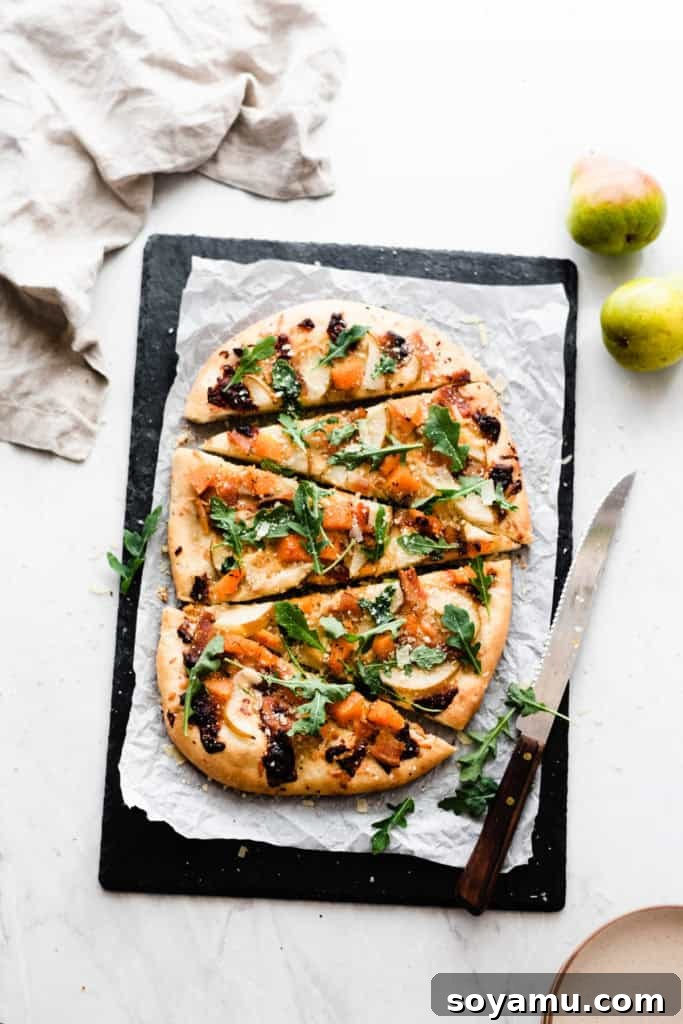 Homemade Pear Pizza with Roasted Butternut Squash, Bacon, and Arugula Sliced up pear pizza on a black cutting stone, showcasing pears, butternut squash, bacon, and arugula.