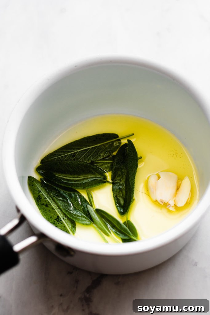 Sage and Garlic Infused Olive Oil for Pizza Olive oil infused with fresh sage leaves and a crushed garlic clove in a small bowl.