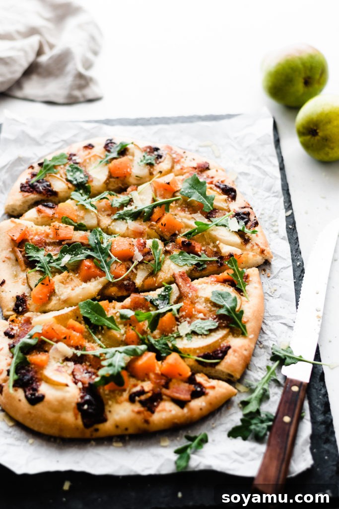 Golden Brown Pear Pizza with Arugula and Parmesan Finished pear pizza sliced on a black cutting stone, topped with fresh arugula and parmesan.