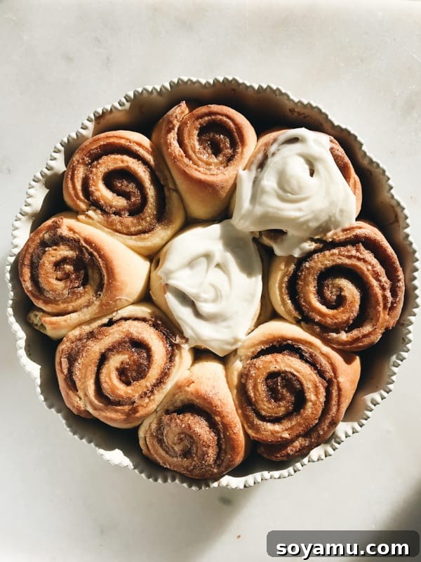 Maple Brioche Cinnamon Rolls Warm maple brioche cinnamon rolls with a generous layer of maple cream cheese frosting, presented beautifully on a serving plate.