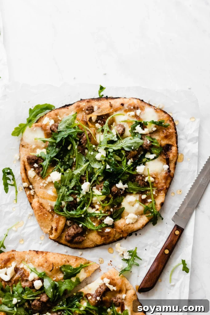 Close-up of a grilled naan bread pizza topped with lamb, caramelized onions, and cheese, before arugula and honey are added