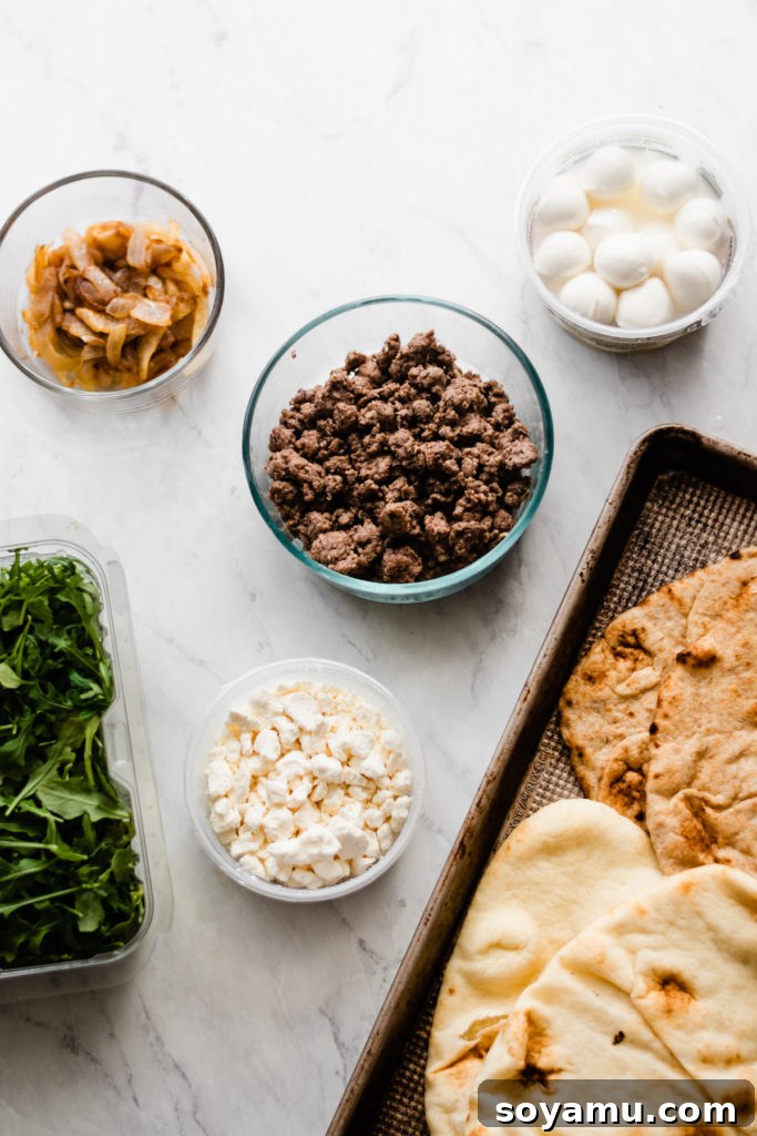 Ingredients laid out for grilled lamb pizzas including naan bread, ground lamb, caramelized onions, cheeses, and fresh arugula