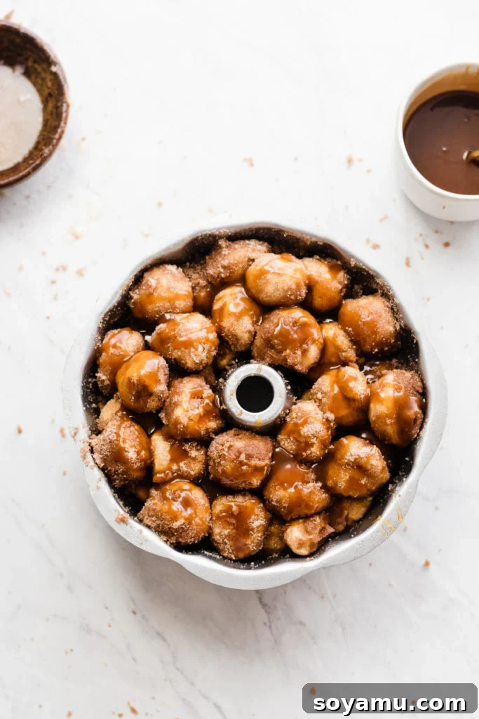 Layers of prepared dough balls and glistening apple cider caramel sauce are carefully stacked within a bundt pan, ready for baking.