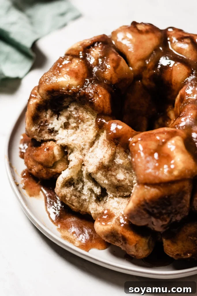 A warm, gooey piece of Caramel Apple Cider Monkey Bread being pulled apart from the main loaf, showcasing its sticky, pull-apart texture.