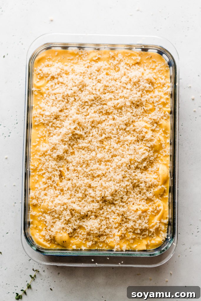 Baked Butternut Squash Mac and Cheese - Incredibly creamy, flavorful, & easy to make! Made with creamy butternut squash sauce, cheddar, parmesan, & smoked gouda cheese, fresh thyme + sage, and a crispy, buttery bread crumb topping. This side will be the star of your Thanksgiving meal! #macandcheese #easyrecipe #vegetarianrecipes #dinnerrecipes #sidedishrecipes #butternutsquashrecipes #thanksgivingrecipes #bluebowlrecipes | bluebowlrecipes.com A pan of unbaked mac and cheese, topped with golden breadcrumbs and ready to go into the oven.