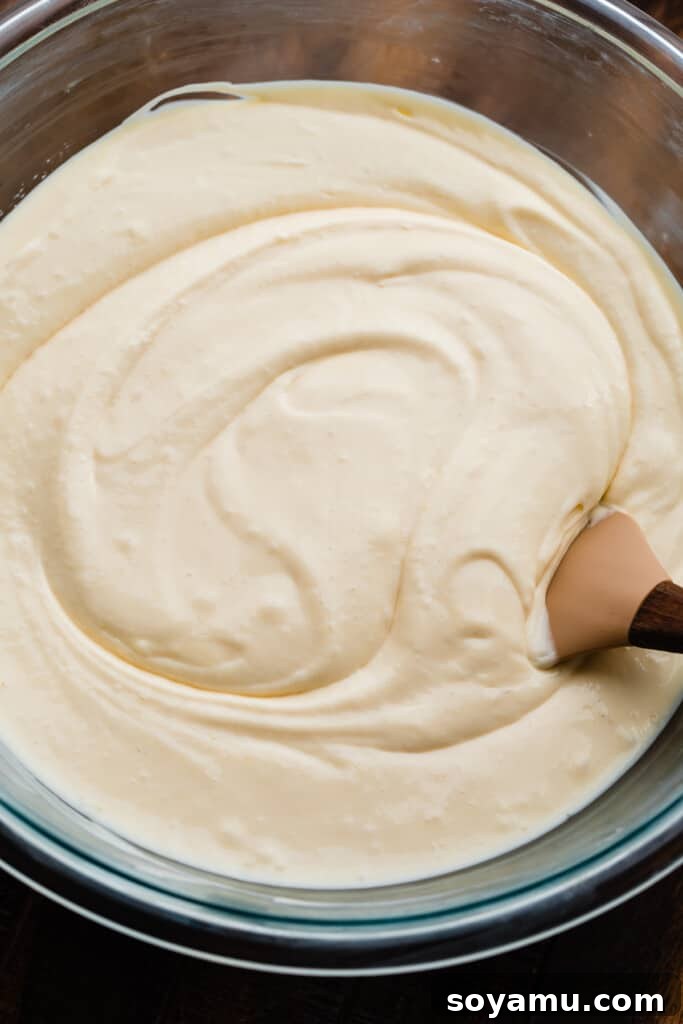 Spiced Pumpkin Swirl Cheesecake with Cookie Butter Crust 2 A large mixing bowl filled with smooth, pale yellow cheesecake batter, showing its creamy and consistent texture before flavor division.