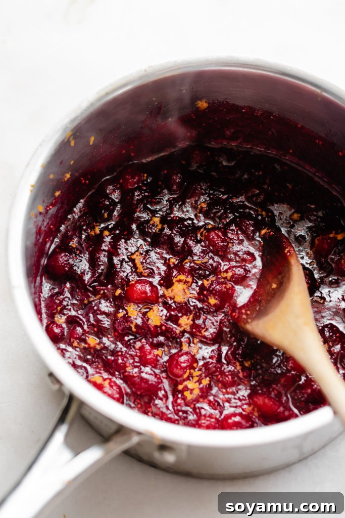 Artisanal Maple Cranberry Sauce 5 A close-up view of the finished homemade cranberry sauce simmering gently in a saucepan, its rich ruby-red color and slightly chunky texture visible, ready for serving.