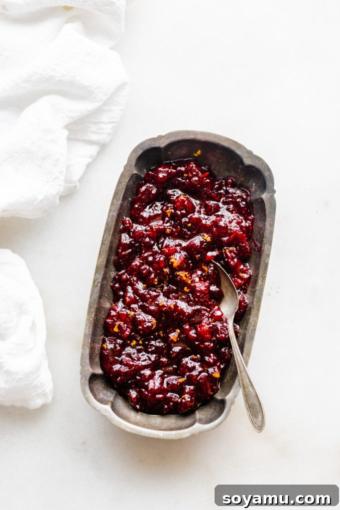 Artisanal Maple Cranberry Sauce 7 A wide-angle shot of a beautifully presented serving dish of homemade cranberry sauce, garnished with fresh orange zest, positioned on a rustic wooden surface, highlighting its vibrant holiday appeal.