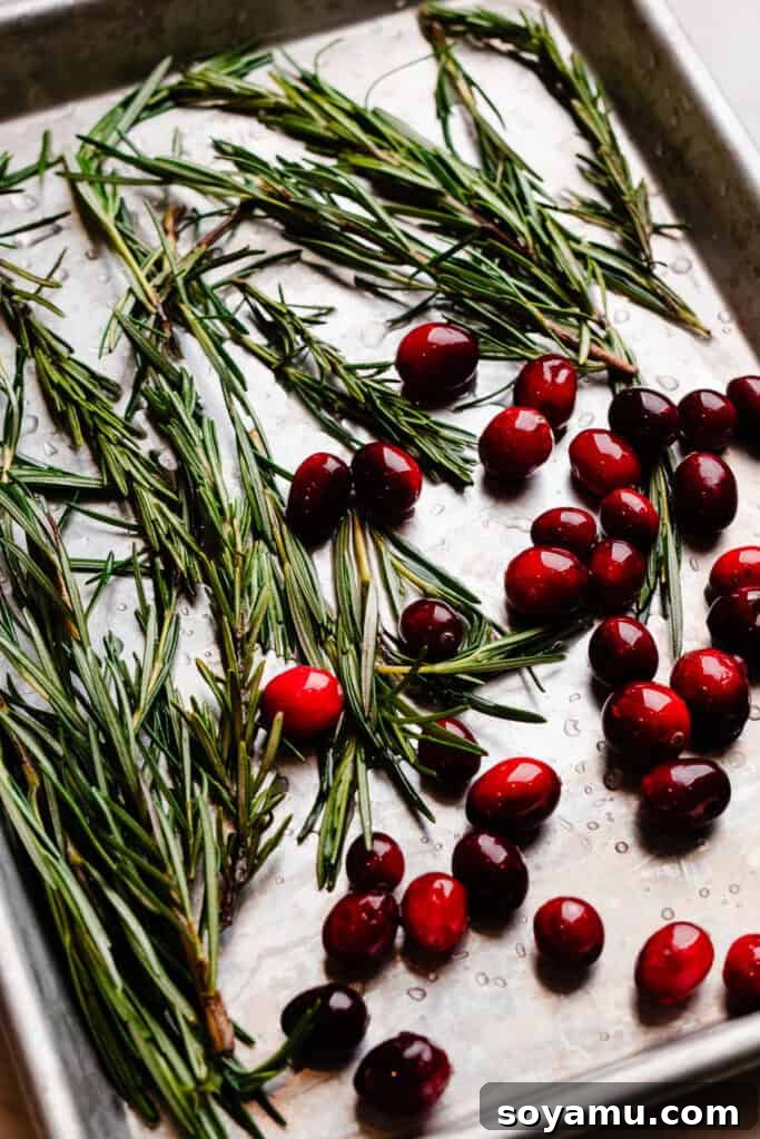 Fresh cranberries and rosemary sprigs coated in simple syrup, laid out on a baking sheet, ready for sugaring.