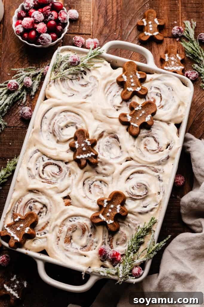 A full pan of beautifully frosted gingerbread cinnamon rolls, ready to be served on a wooden surface.