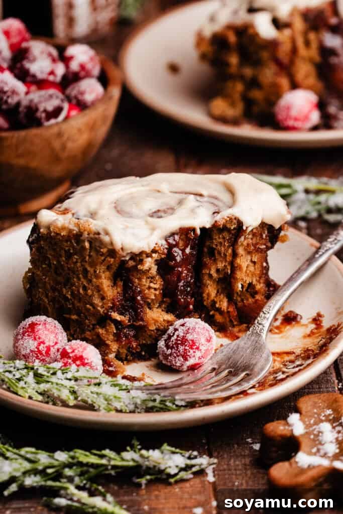 A single gingerbread cinnamon roll on a white plate, showcasing its soft interior and luscious cream cheese frosting, with a few bites missing.