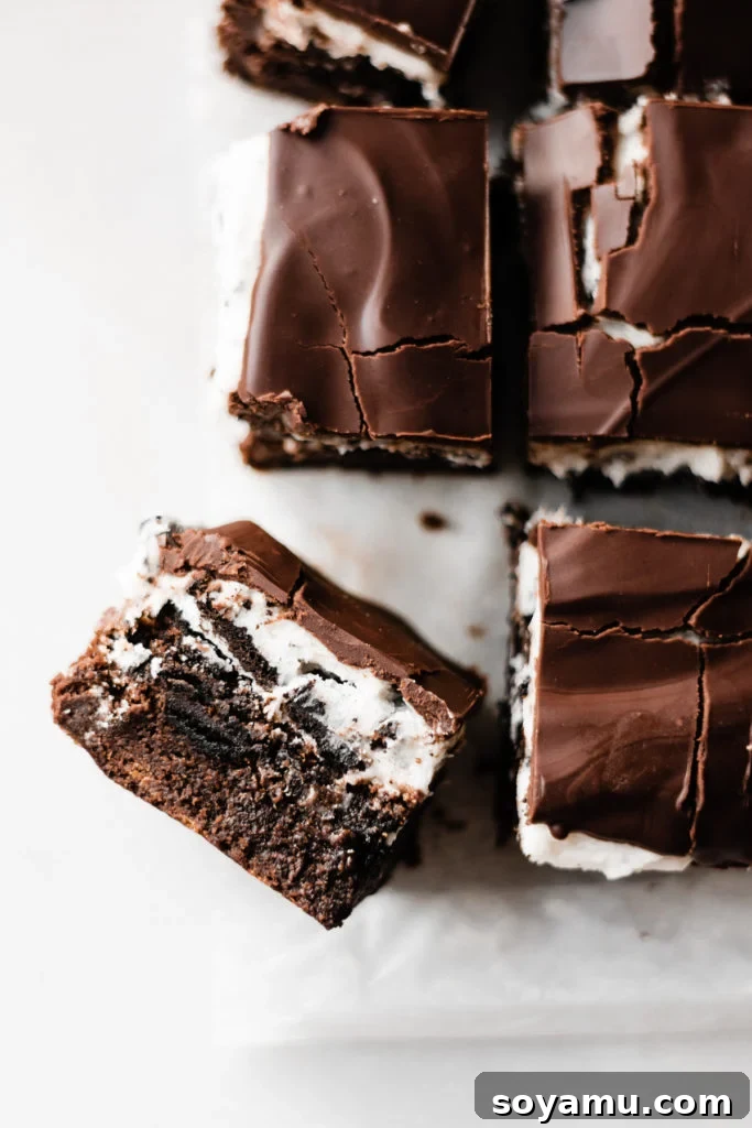 Ultimate Cookies & Cream Bars - The holiday treat to end all holiday treats! Made with a layer of thick, fudgy brownies that have a layer of oreos in the middle, & topped with sweetened condensed milk + crushed oreos. Next up, a layer of oreo frosting and a layer of chocolate to top it all off! This is the stuff of chocolate dreams! #dessertrecipes #christmascookies #brownies #oreo #christmasbaking #christmasrecipes #cookierecipes #frosting #chocolate #bluebowlrecipes | bluebowlrecipes.com A stunning display of sliced Ultimate Cookies & Cream Bars, revealing all the decadent layers. This image captures the rich texture and visual appeal, making them perfect holiday treats for dessert plates and festive gatherings. #holidaytreats #cookiesandcreambars #dessertplatter