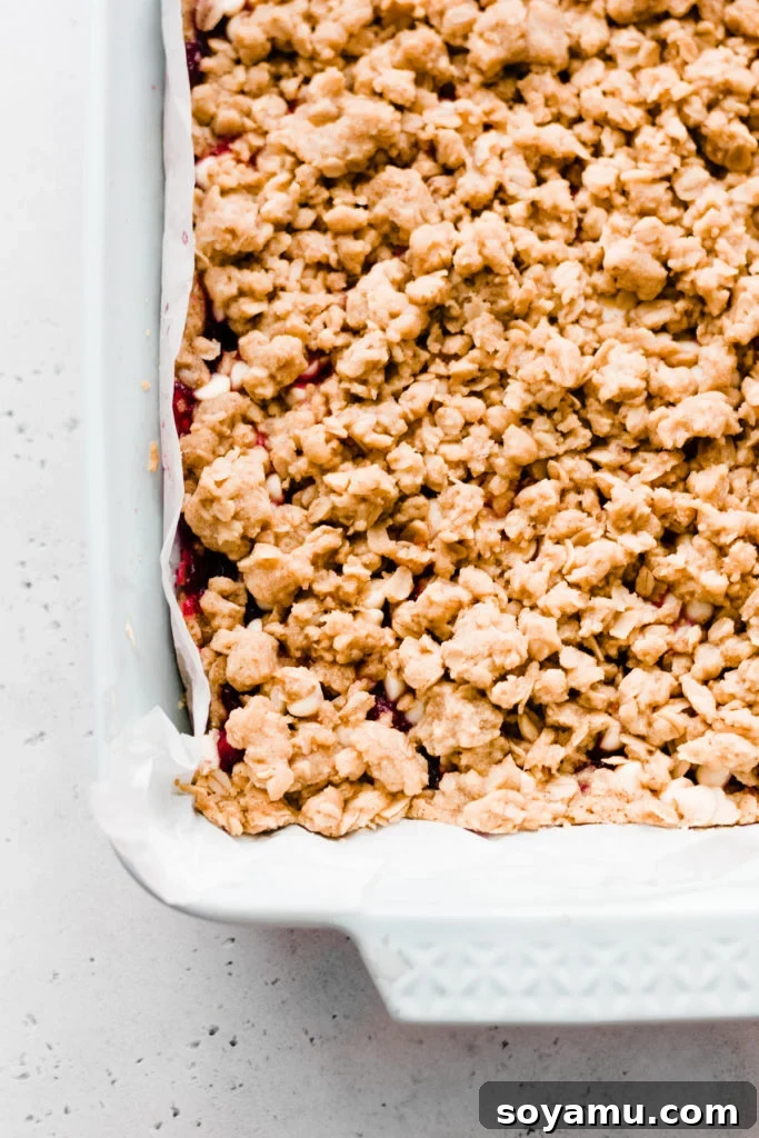 A close-up of the baking pan filled with Cranberry White Chocolate Crumble Bars, featuring the unbaked top crumble layer before returning to the oven.