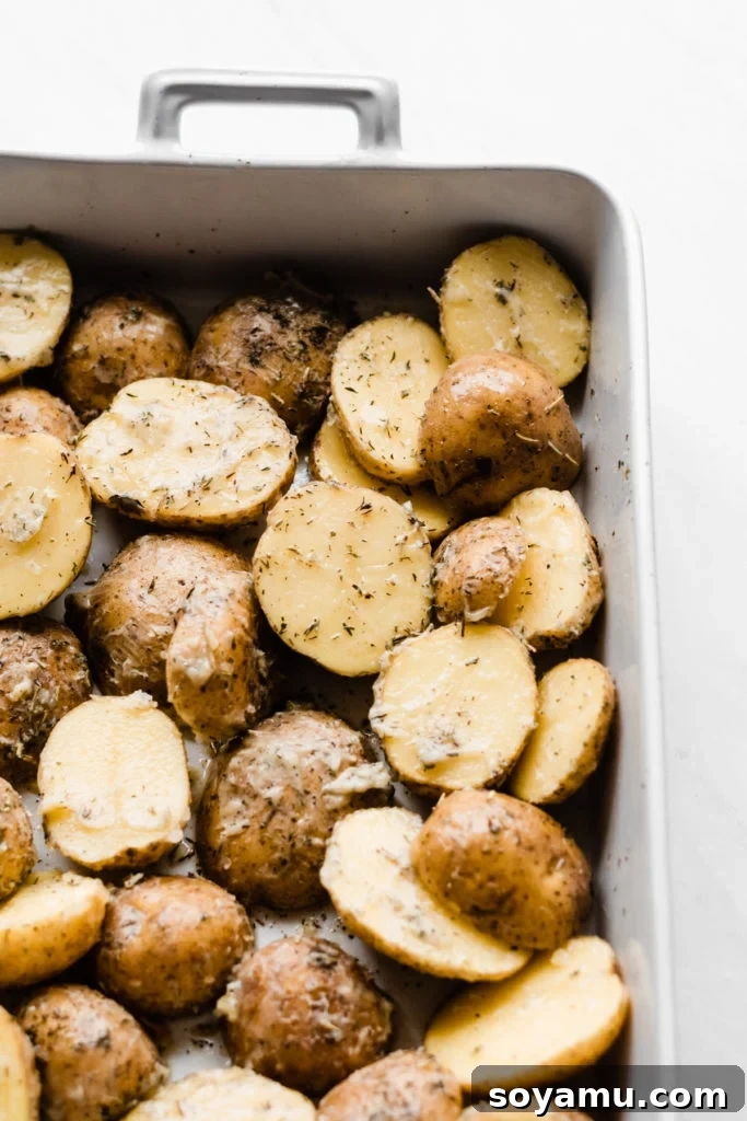 Potatoes tossed with garlic and herb butter, ready for roasting alongside the lamb. Prepping Herbed Garlic Butter Potatoes for the Lamb Roast - Sliced yellow potatoes tossed with melted butter, minced garlic, dried thyme, parsley, and rosemary in a roasting pan, ready to be paired with lamb. Highlights the simple yet essential first step of the recipe. #PotatoRecipe #GarlicPotatoes #HerbButter #RoastingTips #MealPrep #SideDish