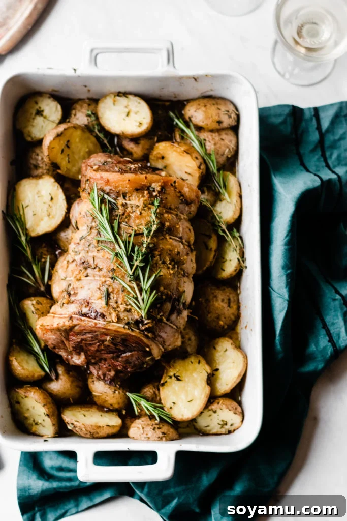 The finished lamb roast and potatoes on a festive table. Herbed Garlic Butter Lamb Roast holiday table setting - A festive holiday table featuring the impressive lamb roast and garlic butter potatoes, surrounded by elegant dishes and seasonal decorations. Highlights the dish as a perfect holiday centerpiece. #HolidayTable #FestiveDinner #GourmetFood #Entertaining #FamilyGathering