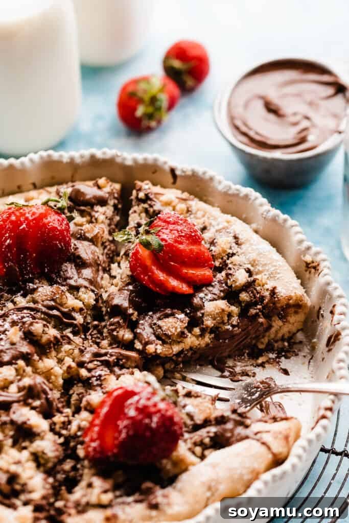 Slices of nutella pizza in a baking dish, drizzled with nutella and topped with fresh strawberries.