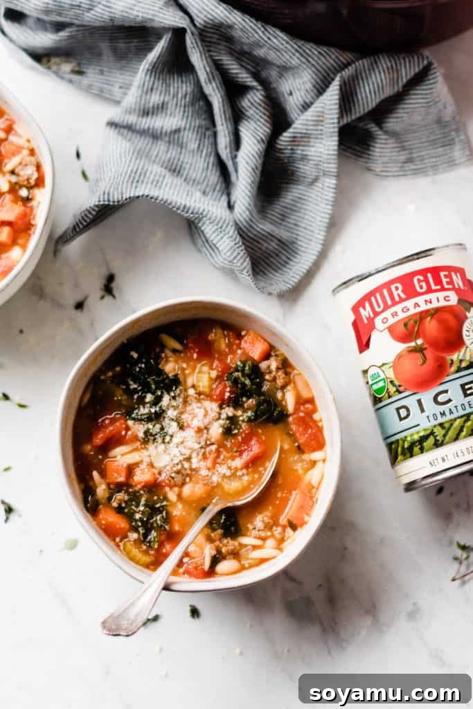 Healthy and Hearty Minestrone Soup - Made with carrots, diced tomatoes, kale, orzo, sausage, and TONS of flavor! This soup is the perfect cold-weather comfort food. It's filling, healthy, tastes incredible, and it's ready in under an hour! #soup #souprecipes #easyrecipes #glutenfreerecipes #minestronesoup #minestrone #winterrecipes #comfortfood #comfortfoodrecipes #healthyrecipes #dinnerrecipes #easyrecipes #easydinner #dairyfreerecipes #bluebowlrecipes | bluebowlrecipes.com White bowl with healthy and hearty minestrone soup, a spoon in the bowl, and a can of diced tomatoes to the side.