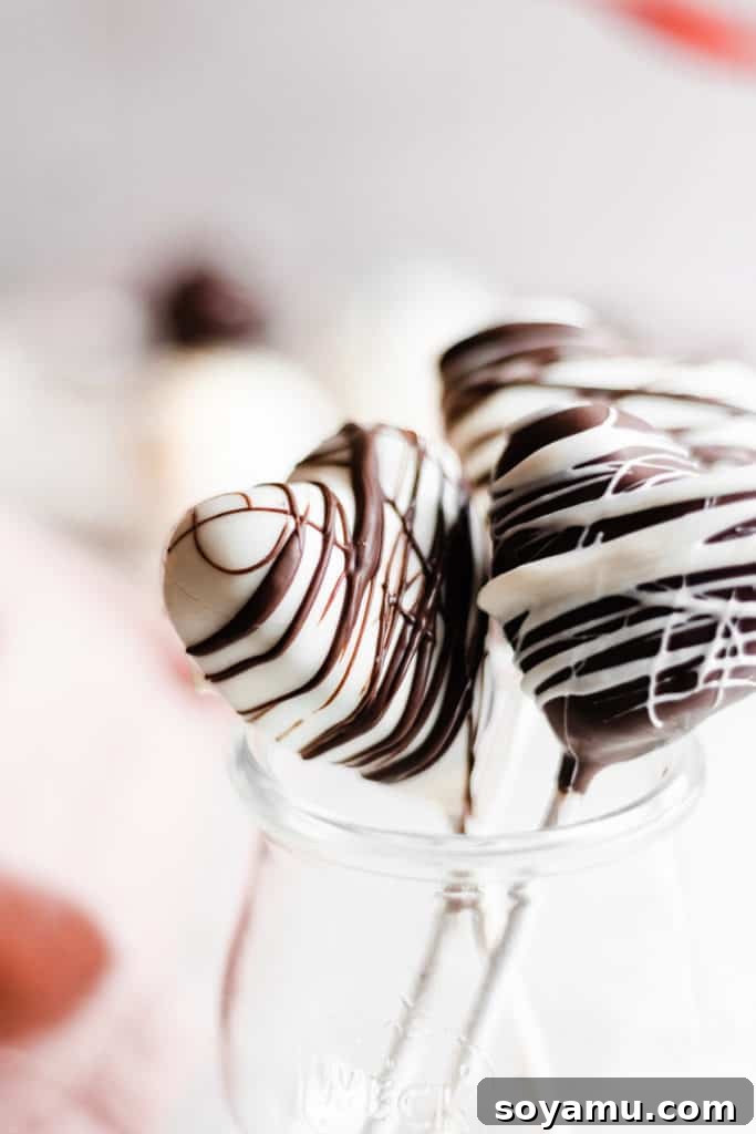 Romantic heart-shaped cake pops for Valentine's Heart-shaped chocolate cake pops, some dipped in white chocolate and others in dark, adorned with drizzles for Valentine's Day.