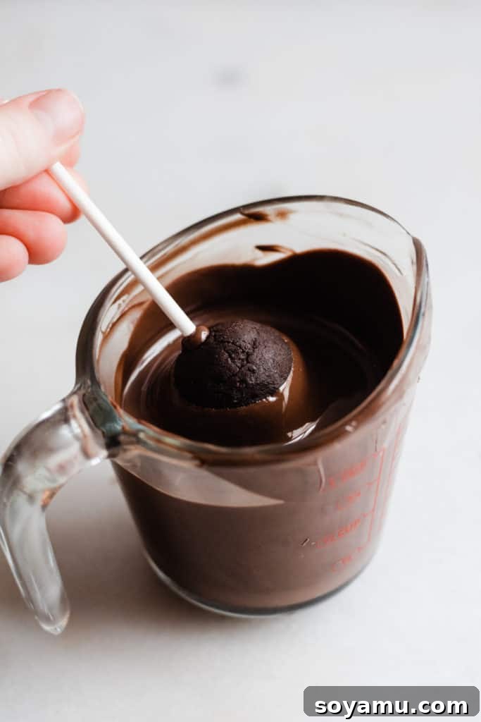 The meticulous process of dipping cake pops for perfection A chocolate cake pop being dipped into melted chocolate for a smooth, glossy finish.