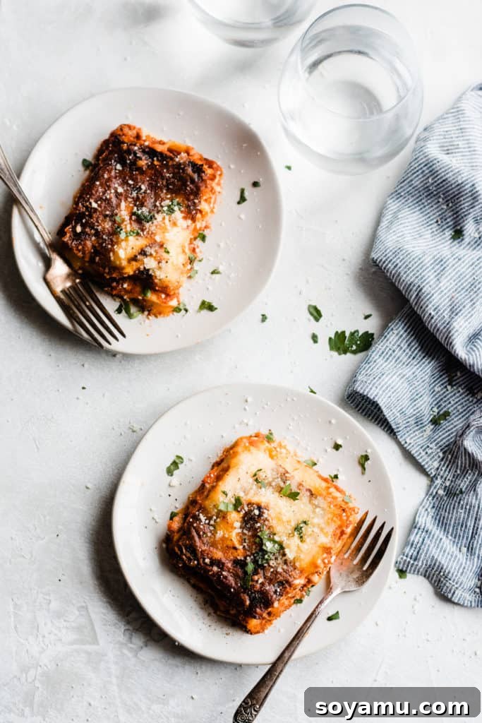 A bird's eye view of two white round plates each with a square of homemade lasagna and a fork on each plate, ready to be enjoyed.