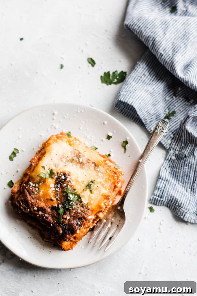 A perfectly portioned serving of homemade lasagna on a white plate, garnished with fresh herbs.