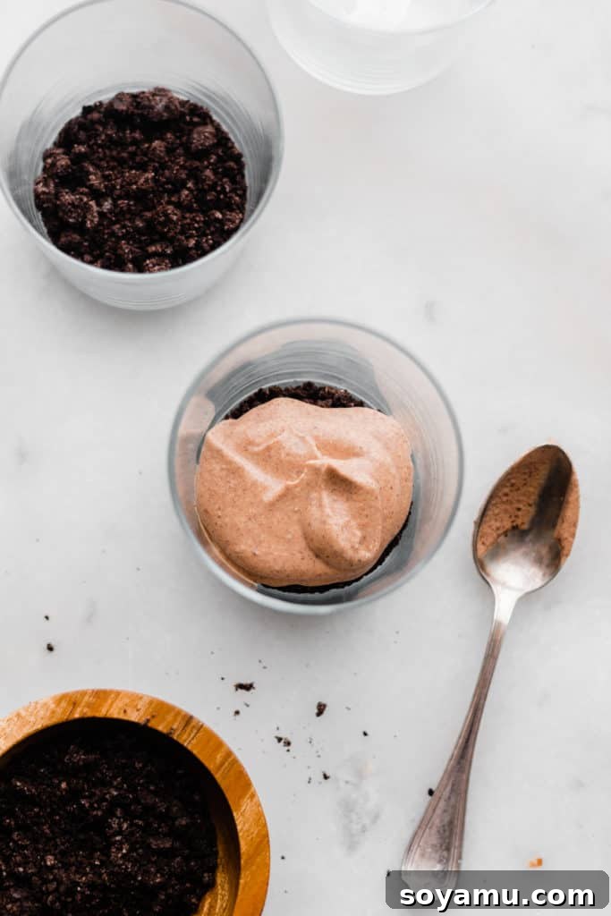 Bailey's Chocolate Mousse Parfaits - Silky smooth layers of Irish cream-infused whipped cream, chocolate whipped cream, and crushed oreos make up these delightful personal-sized desserts! These desserts are so easy to make and are no-bake! Perfect for St. Patrick's Day or any other celebration. Layering crushed Oreos and chocolate cream into a glass for a parfait